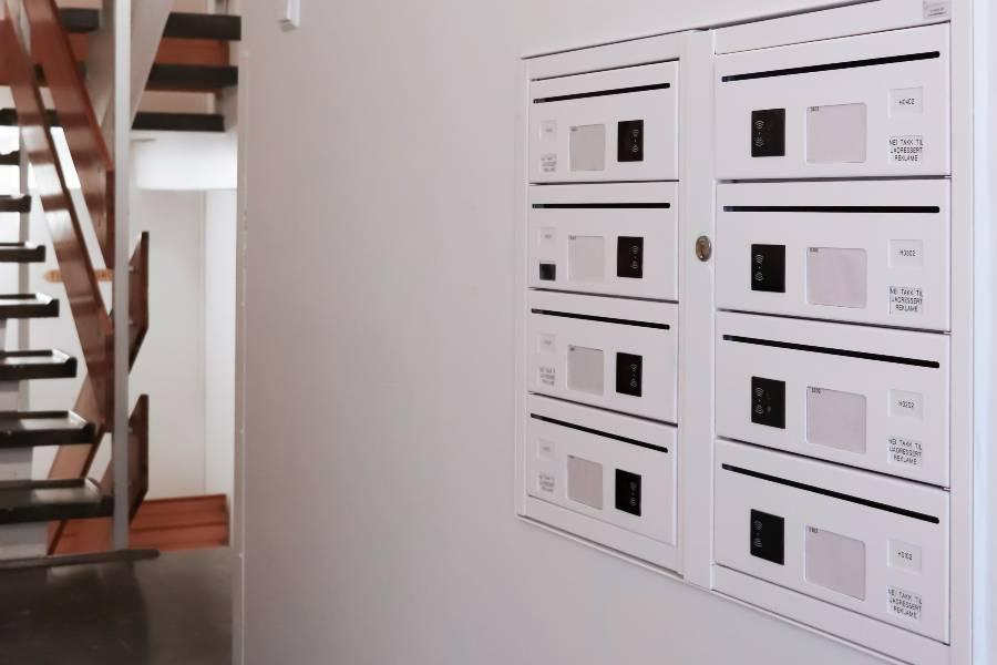 Innendørs postkasser med elektroniske låser innebygget i hvit vegg, trappegang FOTO