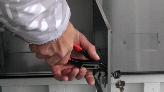 Hender som holder en tang ved en postkassedør med nøkler i låsen FOTO