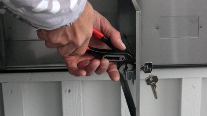 Hender som holder en tang ved en postkassedør med nøkler i låsen FOTO