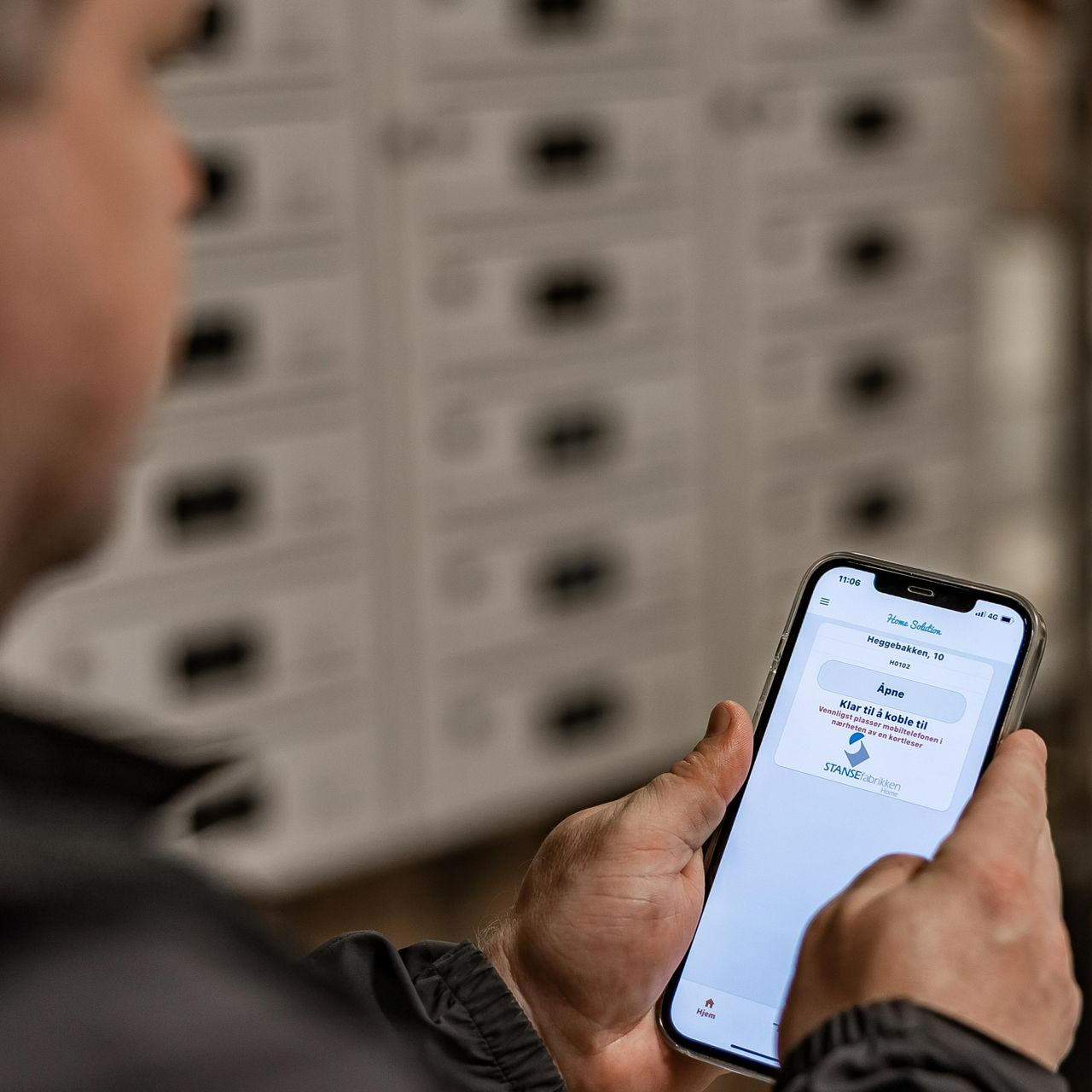 hender som holder en mobiltelefon foran et HomeSoltuion postkasseanlegg fra Stansefabrikken FOTO