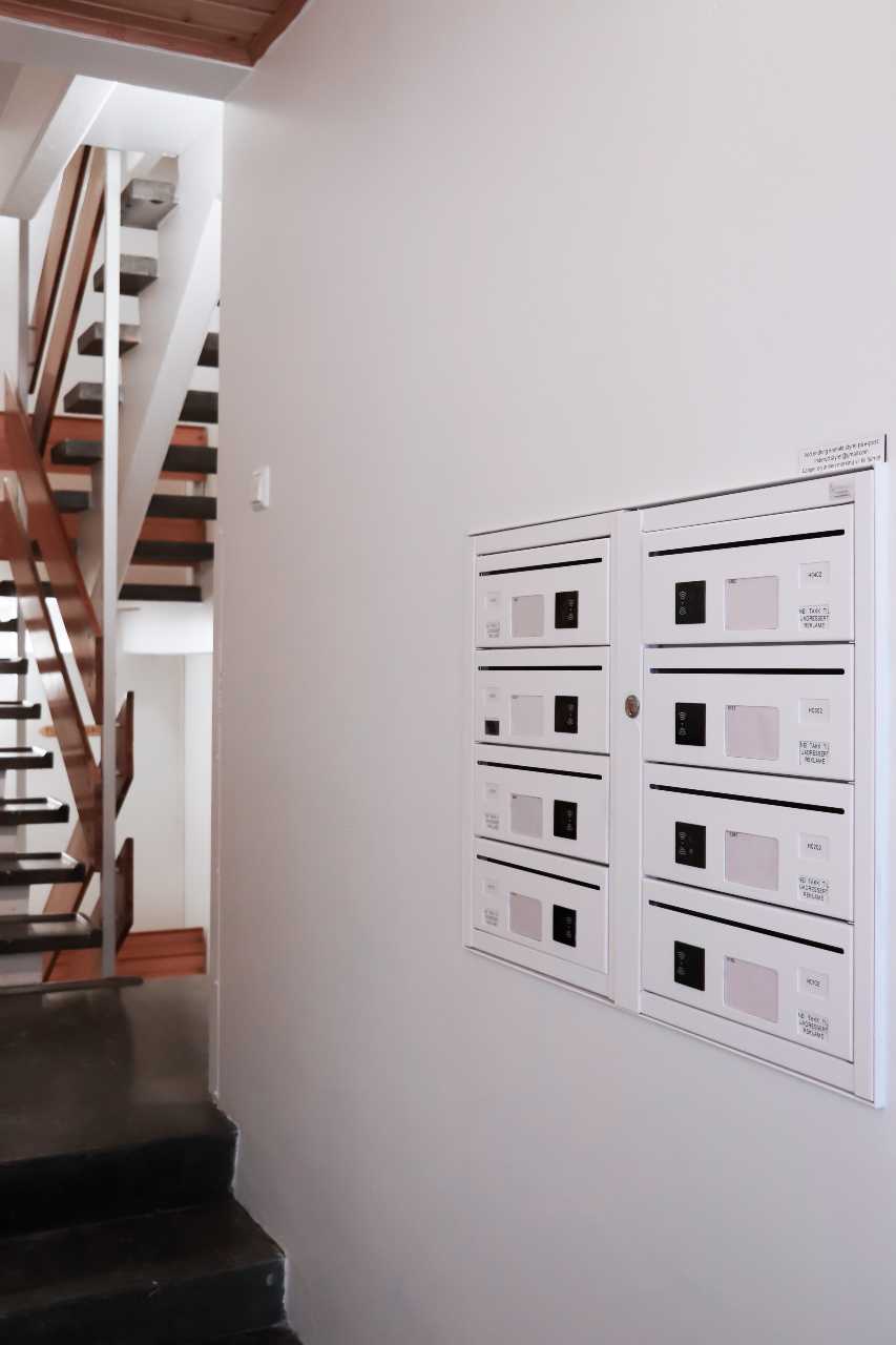 Innendørs postkasser med elektroniske låser innebygget i hvit vegg, trappegang FOTO