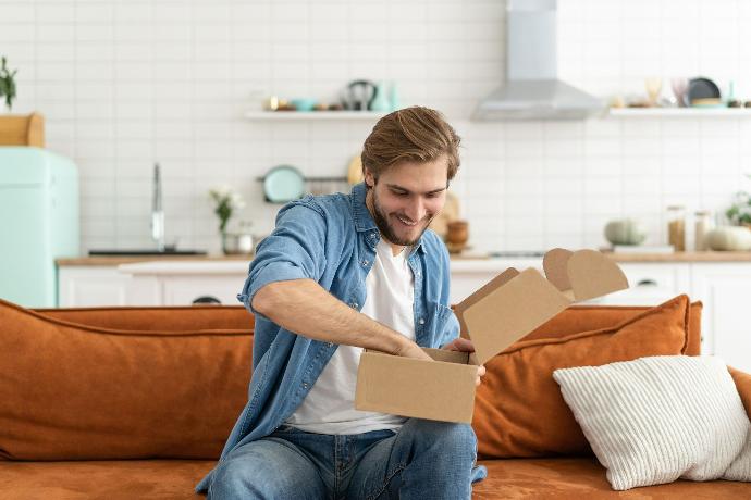 Mann åpner postpakke i sofaen Mann åpner postpakke i sofaen